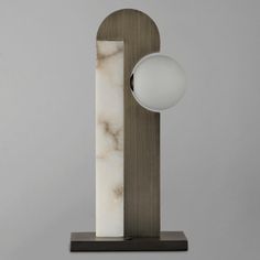 a marble and wood sculpture with a white ball on the base, against a gray background