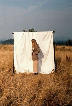 a woman is standing in front of a white sheet on a field with tall grass