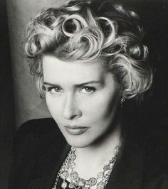 a black and white photo of a woman with curly hair wearing a necklace on her neck