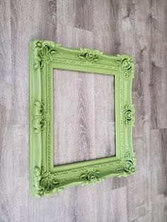 an old green frame on the wall with wood flooring in the background and white paint