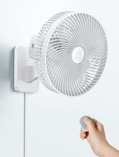 a hand holding a remote control in front of a wall mounted fan