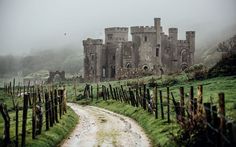 an old stone castle sitting on top of a lush green hillside next to a dirt road