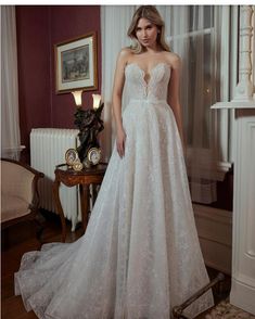 a woman in a wedding dress standing next to a window with her hands on her hips