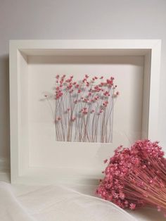 some pink flowers are sitting in a white frame next to a vase with red flowers