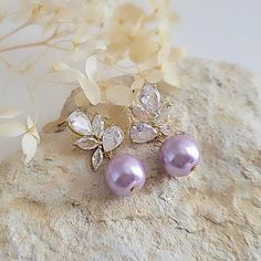 Beautiful Bridesmaid earrings feature an elegant Lavender Glassl pearl drop accompanied by dazzling cz crystals encrusted in gold plating. Simple and visually stunning, this design is the perfect accessory for a modern bride. The Details: * Made with premium quality crystals and lavender glass pearls * Stones are hand set in secure prongs * Great for brides, bridesmaids, mother of the bride, mother of the groom * Great for weddings, engagements, proms, and other special events Perfect earrings f Lavender And Pearl Wedding, Gold Bridesmaid Earrings, Lilac Earrings, Lavender Earrings, Bridesmaid Earrings Gold, Pearl Earrings Wedding, Purple Pearl, Wedding Jewelry Earrings, Pearl Wedding