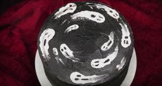 a black cake with white frosting on top sitting on a red cloth covered table