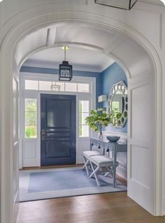 a blue and white entryway with an arch leading to the front door, mirror on the wall