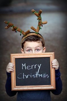 a young boy holding up a chalk board with reindeer antlers on it's head