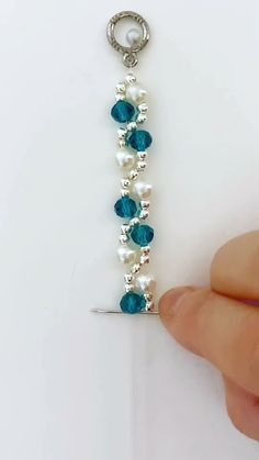 a person is holding a piece of jewelry with pearls and blue glass beads on it