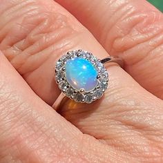 a woman's hand holding an opal and diamond ring