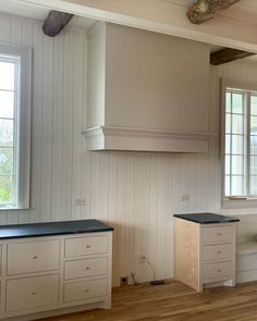 an empty kitchen with white cabinets and black counter tops in front of two large windows