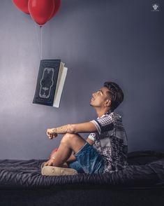 a young boy sitting on a bed with two red balloons attached to the wall above him