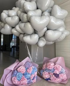 two bouquets of flowers are in front of a large bunch of white and pink balloons