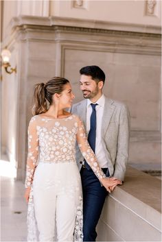 a man and woman standing next to each other in front of a stone wall holding hands