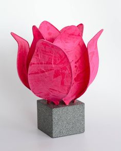 a pink paper flower sitting on top of a block of cement in front of a white background