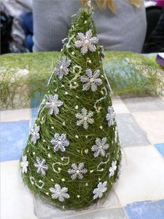 a small christmas tree made out of grass and white snowflakes sits on a checkered tablecloth