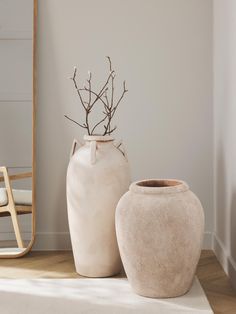 two white vases sitting next to each other on a wooden floor in front of a mirror