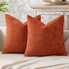 two orange pillows sitting on top of a white couch next to a potted plant