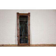 an old wooden window sitting in front of a white brick wall on a wood floor