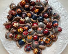 a white plate topped with lots of different types of painted glass balls on top of a table