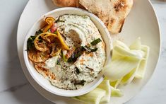 a white bowl filled with hummus and vegetables next to some bread on a plate