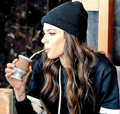 a woman drinking from a cup while wearing a beanie