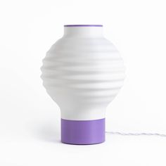 a white and purple vase sitting on top of a table next to a power cord