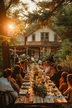 a group of people sitting around a long table with food on it in front of a house