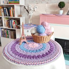 a crocheted basket with balls of yarn sitting on top of it in front of a bookshelf