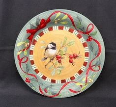 a decorative plate with a bird painted on the front and red ribbon around it's edge