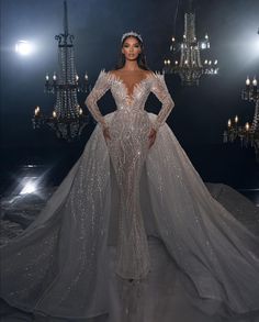 a woman in a wedding dress standing on a runway with chandeliers behind her