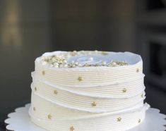 a white cake with gold stars and pearls on it's top is sitting on a plate