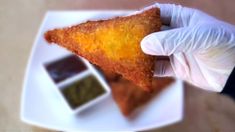 a person in white gloves holding up a piece of food with dipping sauce on it