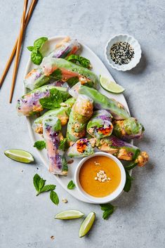 a white plate topped with vegetables covered in sauce next to chopsticks and dipping sauce