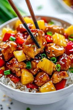 a white bowl filled with chicken, pineapples and rice topped with chopsticks