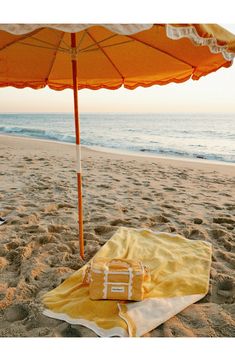 an orange umbrella and yellow blanket on the sand at the beach with water in the background