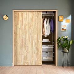 an open wooden closet with clothes hanging on the wall and drawers below it, next to a potted plant