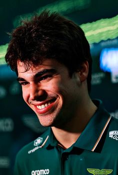 a smiling man wearing a green shirt and black collared shirt smiles at the camera