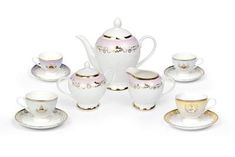 a white tea set with gold trimmings on the rim and saucers in front of it