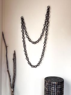 a chain is hanging on the wall next to a black vase and tree branch sculpture