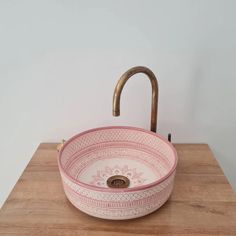 a pink and white bowl shaped sink sitting on top of a wooden counter next to a faucet