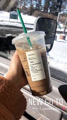 a person holding up a cup with a straw in it on the dashboard of a car