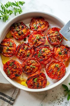 a white bowl filled with sliced tomatoes on top of a table next to a knife