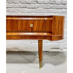 a wooden desk with brass legs and a drawer on the top, in front of a white brick wall