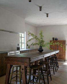 an empty kitchen with stools and a table in the center, surrounded by plants