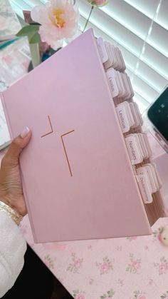 a person holding up a pink box with chocolates in it on a table next to flowers