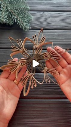 two hands are holding an ornament made out of wood and paper with the shape of a flower