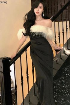 a woman in a black and white dress is standing on the stairs with a glass of wine