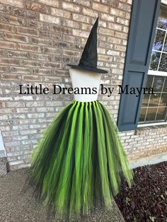 a green and black dress with a witches hat on it, sitting in front of a brick building