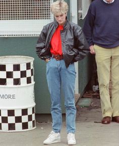 a woman standing next to a man in front of a building wearing a black jacket and red shirt